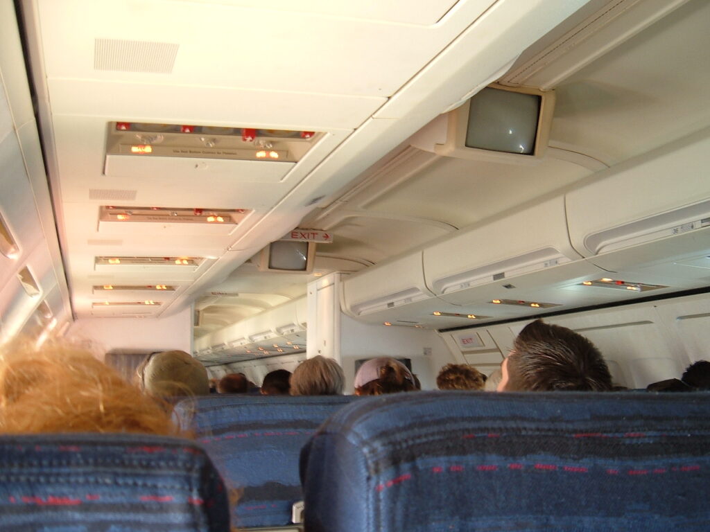 View of the cabin from the passenger perspective. Note the CRT monitors in the ceiling, and the cloth material for the seats.